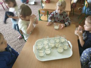 Dzieci siedzą przy stoliku, na którym stoi taca ze szklankami i koktajlem. Dzieci częstują się.