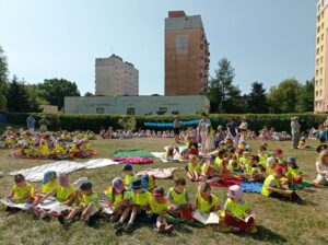 na dużym placu trawy siedzi duża grupa dzieci