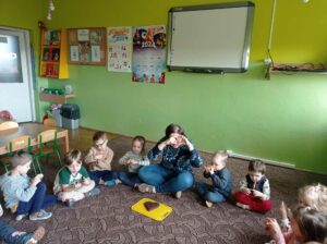 nauczycielka siedzi na dywanie z dziećmi, pokazuje jak zrobić serce z dłoni