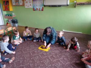 nauczycielka siedzi na dywanie z dziećmi, kroi na desce czekoladowe serce