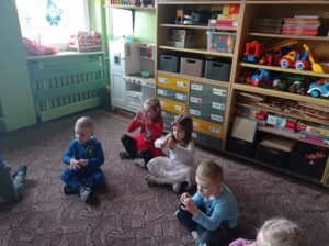 pięcioro dzieci siedzi na dywanie, robią serce z dłoni