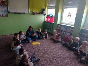 grupa dzieci siedzi w sali przedszkolnej z panią, na dywanie deska do krojenia