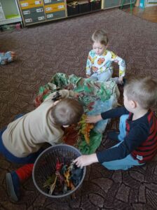 Troje dzieci bawi sie na dywanie dinozaurami