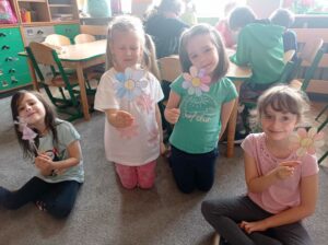 cztery dziewczynki klęczą na dywanie, w ręku trzymają papierowe kwiaty