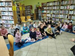 Dzieci siedzą na macie w bibliotece.