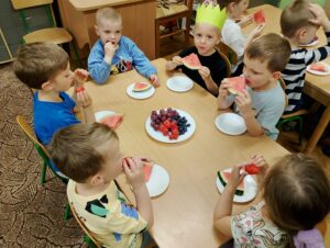 Dzieci siedzą przy stolikach i jedzą owoce