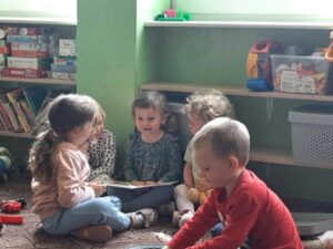 grupa dzieci siedzi w kole, obok chłopiec bawi się 