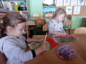 dwie dziewczynki siedzą przy stoliku i malują farbami