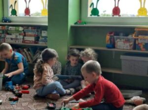 grupa dzieci siedzi na dywanie, dziewczynka trzyma książkę