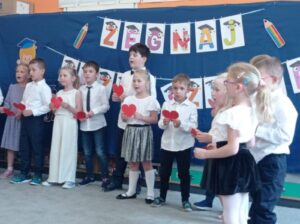 grupa dzieci w strojach galowych stoi przed dekoracją