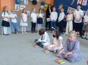 troje dzieci gra na dzwonkach, z tyłu grupa dzieci