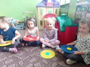 grupa dzieci siedzi na dywanie, przed nimi krążki