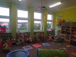 grupa dzieci siedzi w sali, na dywanie rzeczy do ćwiczeń