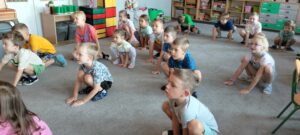 Dzieci kucają na dywanie jak żabki