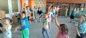 Dzieci stoją na dywanie i wykonują krążenia ramion w przód