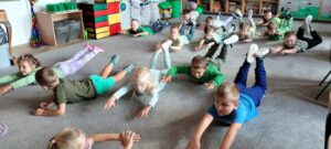 Dzieci leżą na dywanie na brzuchu z uniesionymi rękoma i nogami