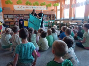 grupa dzieci siedzi na dywanie, przed nimi dwie aktorki