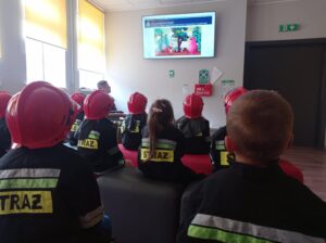 grupa dzieci siedzi w strojach strażaków i ogląda prezentację
