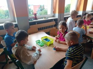 grupa dzieci siedzi przy stoliku i robi kulki z bibuły