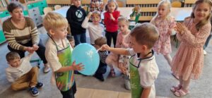 Dwóch chłopców goli balon, pozostałe dzieci przyglądają się.