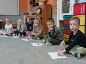 dzieci mają przed sobą karty pracy, w ręku pionki