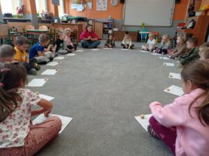 dzieci siedzą w kole, przed nimi karty pracy