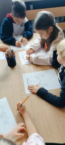 Dzieci siedzą przy stolikach i wypełniają karte pracy