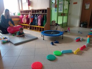 na holu rozłożona jest trampolina, ścieżka sensoryczna, materac, dziecko ćwiczy 
