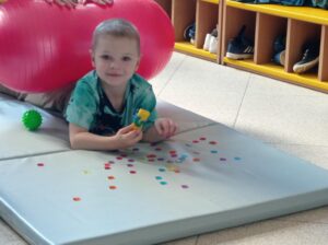 dziecko leży na materacu i zbiera kolorowe guziki