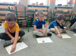 troje chłopców trzyma pionki i przesuwają po kartach pracy