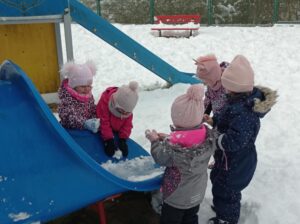 dzieci stoją obok zaśnieżonej zjeżdżalni