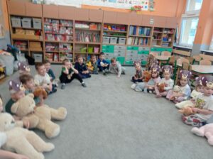 grupa dzieci siedzi w kole w sali, w rękach trzymają misie