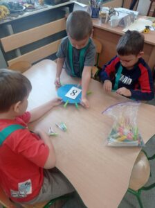 troje dzieci przyczepia osiem klamerek do krążka