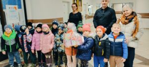 Dzieci pozują do zdjęcia z paczką herbat oraz dorosłymi z DPS