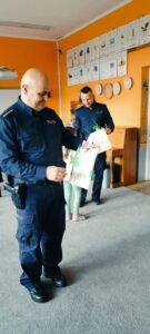 Dzieci wręczaja policjantom podziękowania i papierowe kwiatki