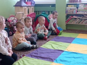 grupa chłopców siedzi przed kolorowym dywanem, chłopiec rzuca kostką