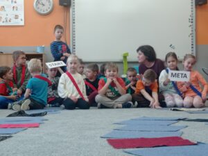 pani z grupą dzieci, przed nimi pola gry zrobione z materiałowych prostokątów