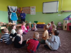 dzieci siedzą na dywanie, do sali wchodzi Kicia Kocia i pracownik księgarni