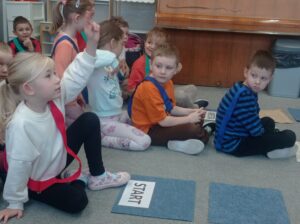 grupa dzieci siedzi na dywanie, dziewczynka zgłasza się