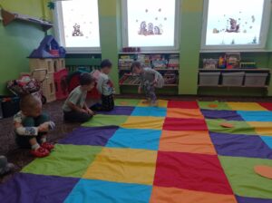 dziewczynka skacze po kolorowych polach, grupa dzieci patrzy