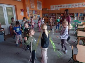 grupa dzieci stoi na dywanie, w ręku wstążki