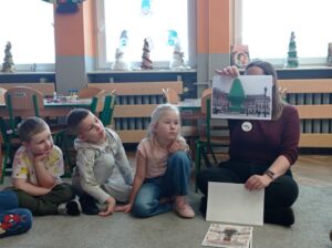 pracownik BWA pokazuje dzieciom obrazki z choinkami