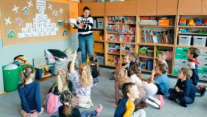 Dzieci siedzą przed tablicą na której jest kalendarz adwentowy z zadaniami