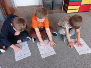 dzieci siedzą na dywanie, wodzą palcem po obrazku