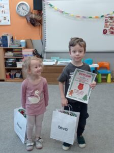 dziewczynka patrzy na chłopca trzymającego dyplom