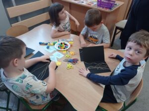 czworo dzieci przy stoliku przewdziewa sznurek