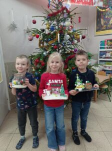troje dzieci stoi przed choinką, trzyma w ręku prace wykonane na konkurs