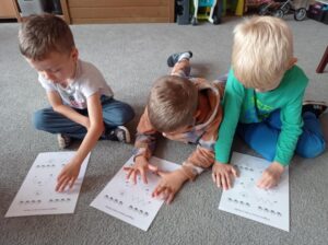 dzieci siedzą na dywanie, wodzą palcem po obrazku