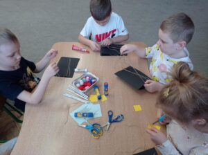 dzieci przy stoliku wycinają elementy prac